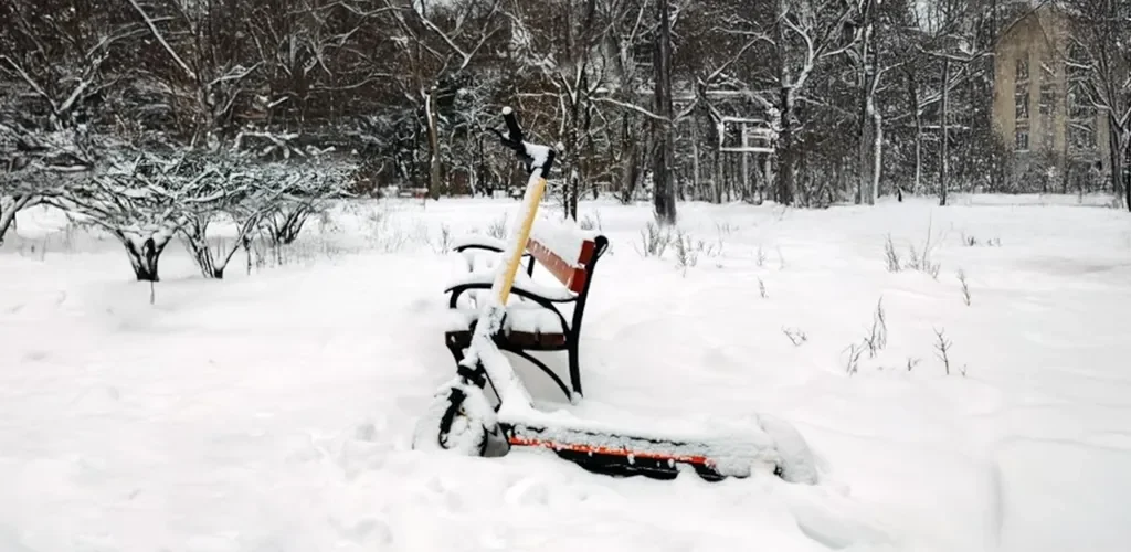 A rental scooter covered in snow leaning towards a bench
